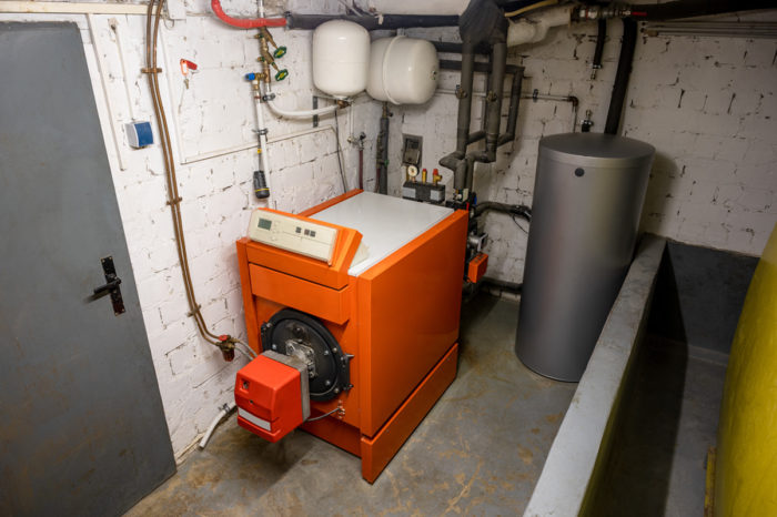 Ancien système de chauffage au fioul avec une cuve à fioul et un ballon d'eau chaude dans le sous-sol d'une maison - chauffage aux combustibles fossiles