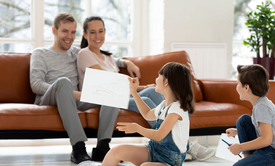 couple sur un canapé avec des enfants qui jouent au sol au premier plan et un radiateur à inertie en arrière plan